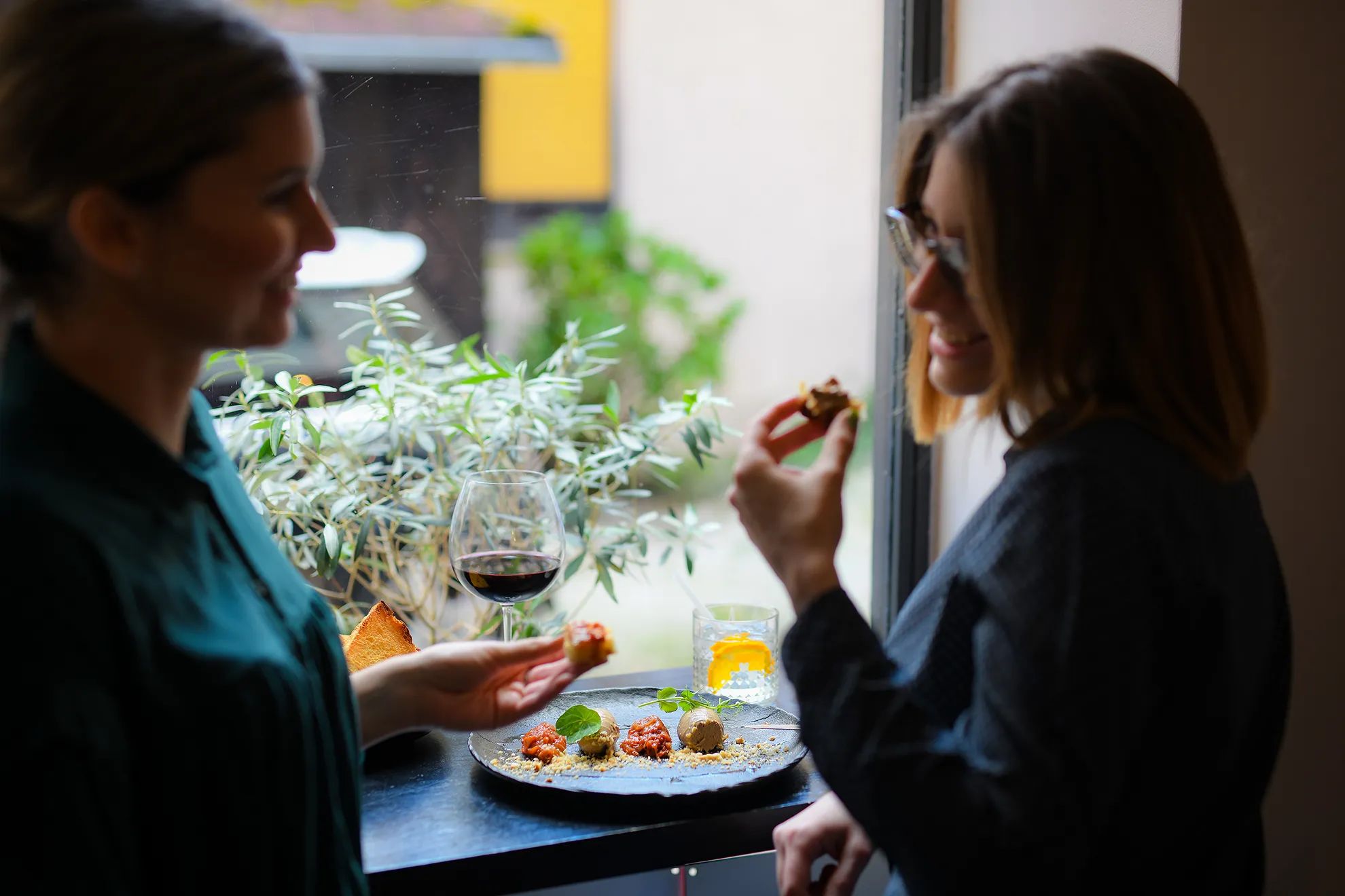 Otvori fotografiju: Dvoje gostiju dijeli zalogaje za stolom uz prozor, uz čašu crnog vina (15/18)